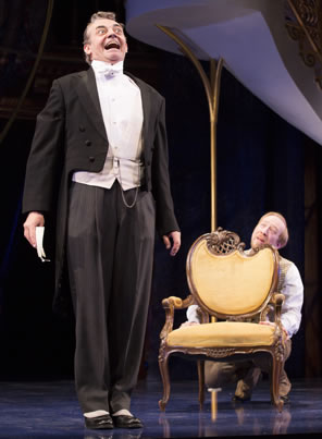 In tux and tales, letter in right hand, Malvolio smiles maniacally as Aguecheek hides behind a regency style chair