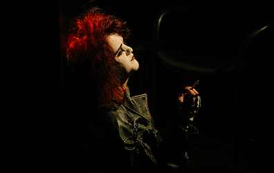 SIG-This_Ends_In_Blood-Witch-3 First Witch looks up with bright red hair and stark makeup, wearing a black leather jacket, and a cigeratte in her fingerless-gloved right hand.