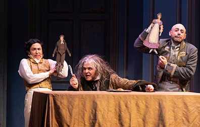 Production photo of scraggly haired Sir Pit Crawley brandishes a butter knife as other actors hold up stick puppets behind him.